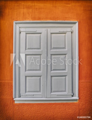 Picture of grey closed shutters window on vibrant orange wall filtered